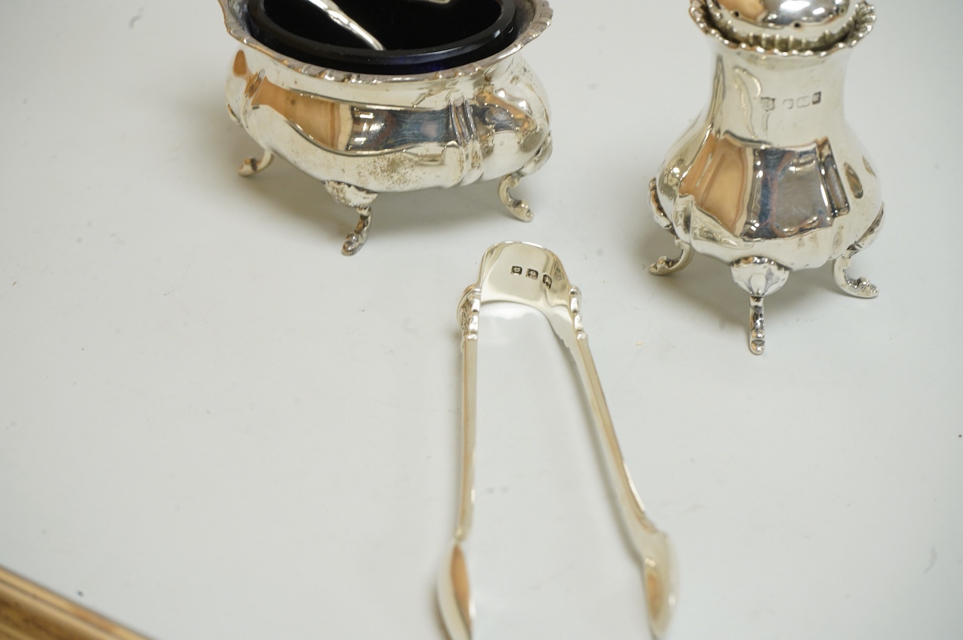 A George V silver sauceboat by Mappin & Webb, Birmingham, 1933, length 16.2cm, together with a silver salt and spoon, with blue glass liner, a silver pepperette, a pair of silver sugar tongs and a Spanish white metal two